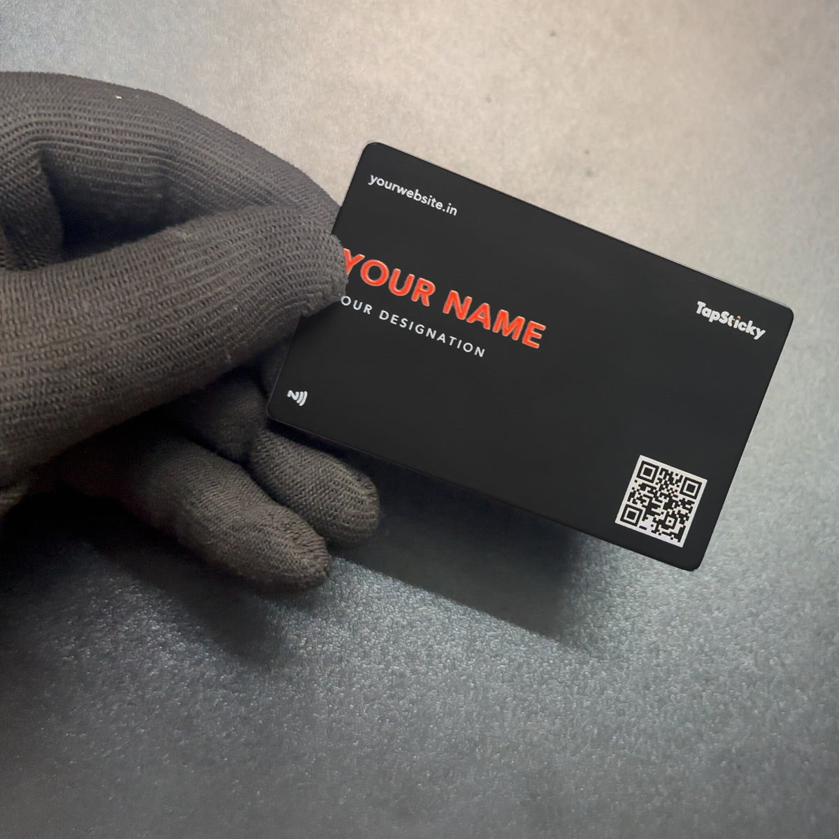 Black metal NFC business card with a red printed name and a QR code, held in a gloved hand